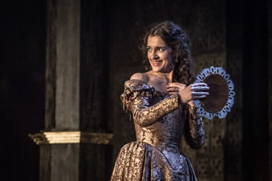 Jessica in gold embroidered dress and holding a tamborine type intestrument as she smiles looking over her right shoulder